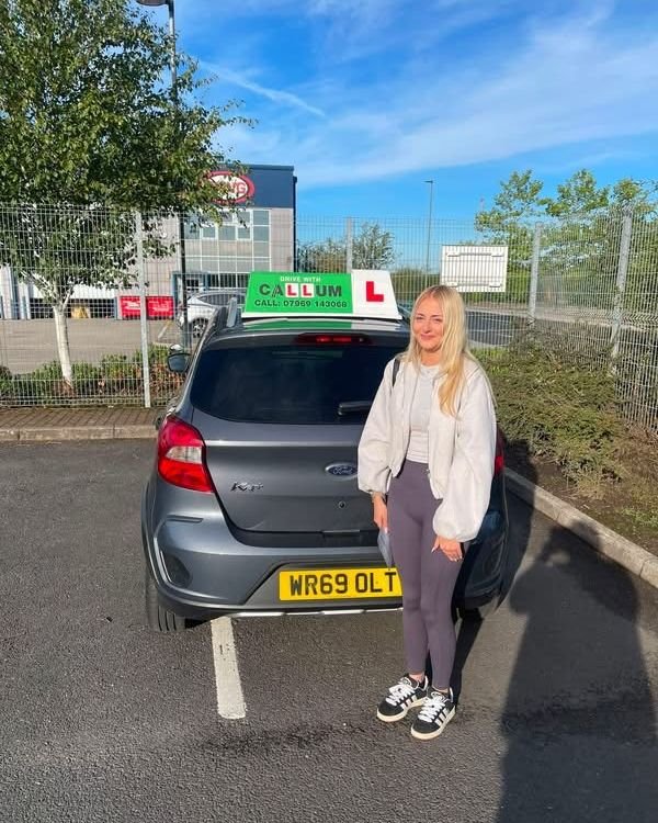 A pupil celebrating passing their driving test beside the Drive With Callum car