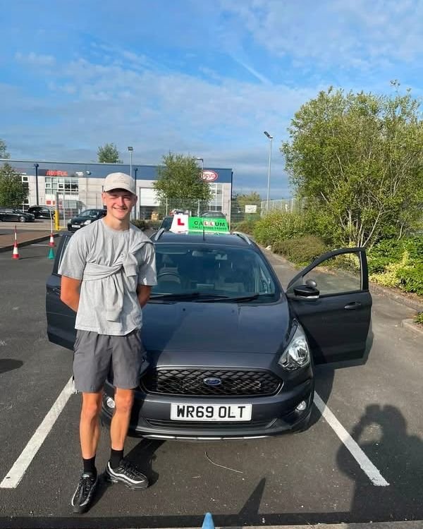 A pupil celebrating passing their driving test beside the Drive With Callum car