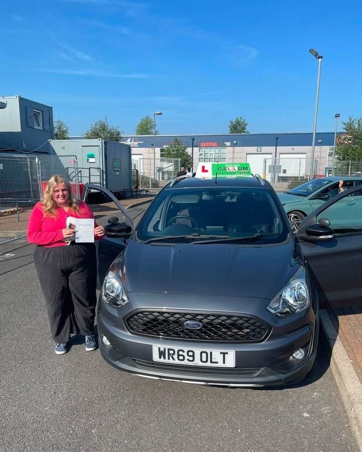 A pupil celebrating passing their driving test beside the Drive With Callum car