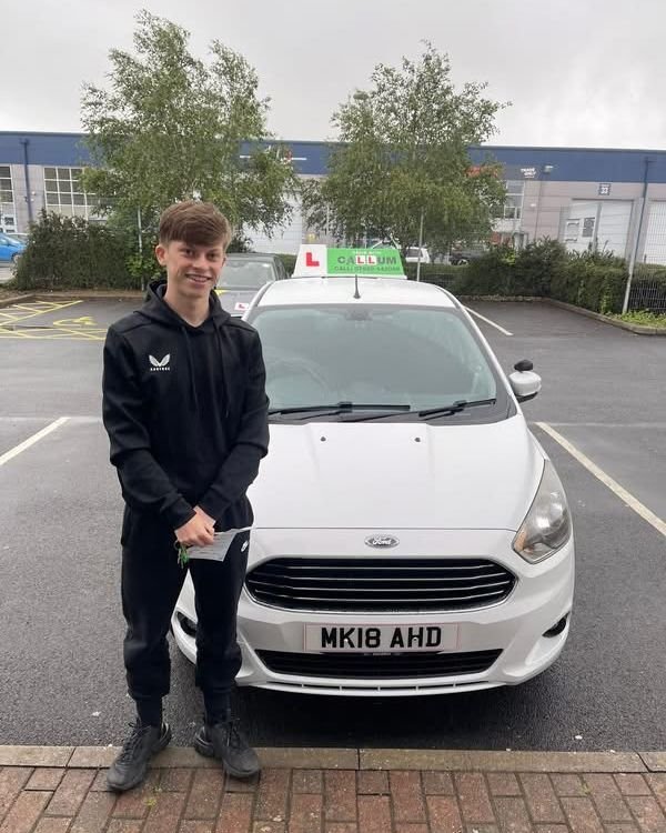 A pupil celebrating passing their driving test beside the Drive With Callum car