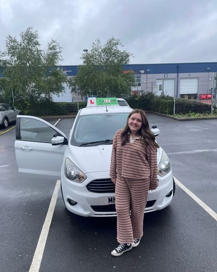 A pupil celebrating passing their driving test beside the Drive With Callum car