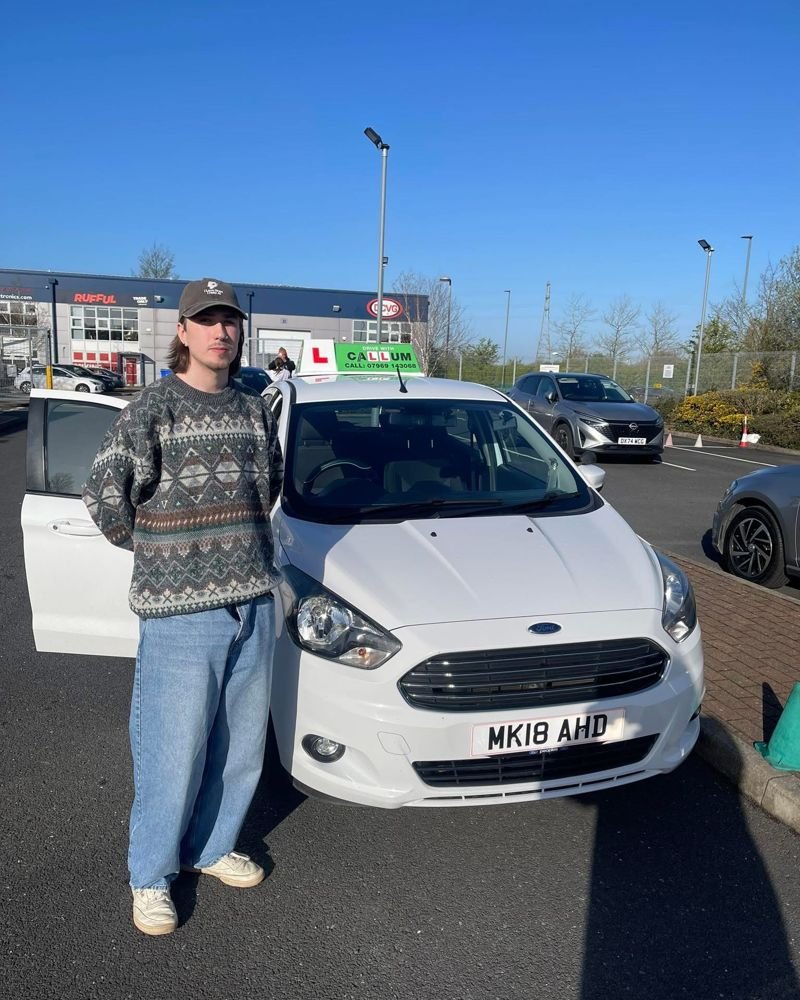 A pupil celebrating passing their driving test beside the Drive With Callum car
