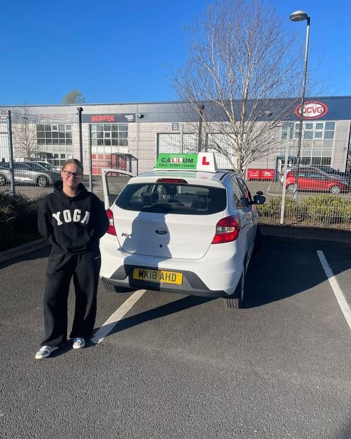 A pupil celebrating passing their driving test beside the Drive With Callum car